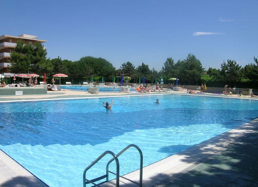 Residence Valbella in Bibione: outdoor hotel pool with swimmers, sun loungers, and trees