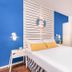 Gesher Haziv Travelhotel room in Nahariyya with blue accents, striped headboard and a wall-mounted TV