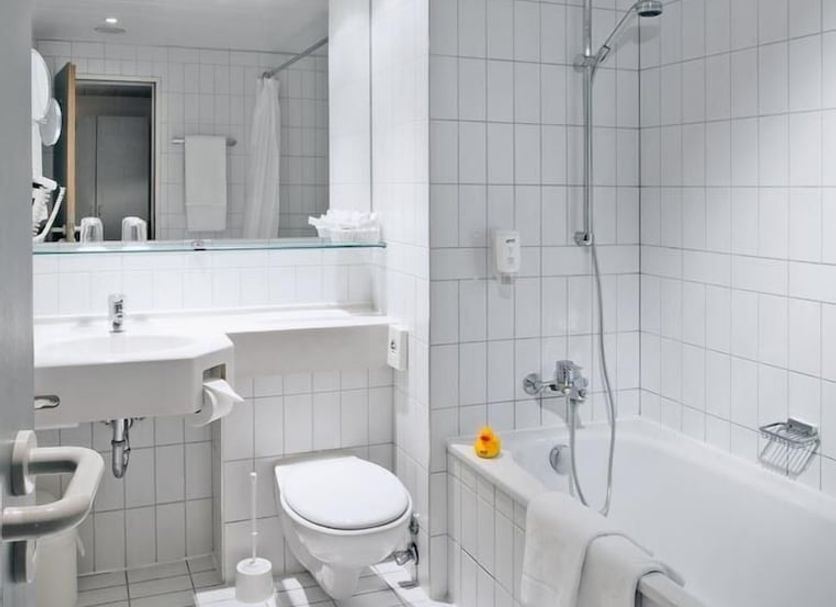 Wyndham Garden Düsseldorf Mettmann bathroom with bathtub, shower, sink, toilet, and white tile walls in Mettmann