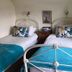 West Lodge Hotel in Aylesbury: twin room with two white metal beds, teal throws, and a window with curtains.