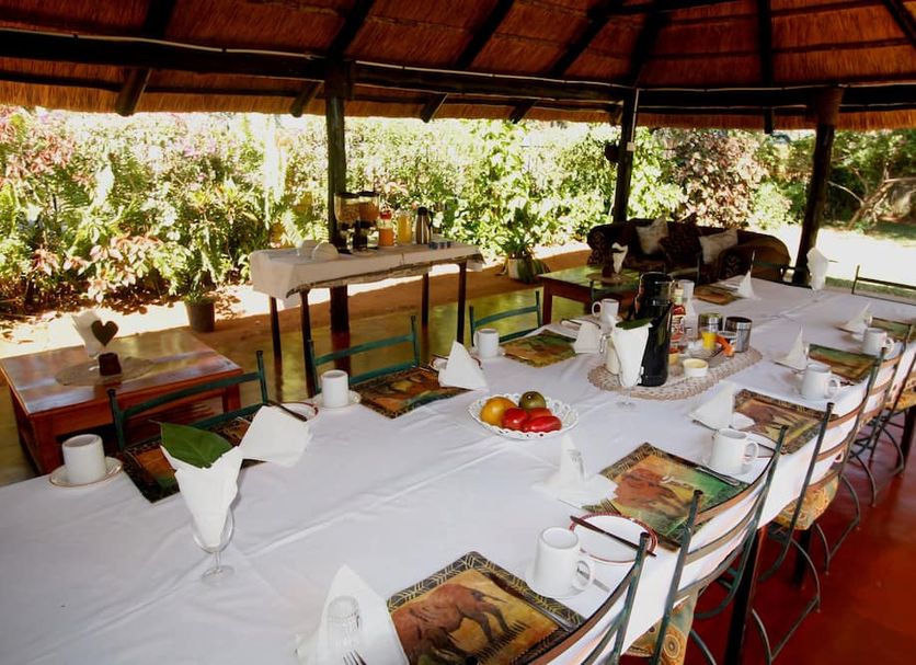 Wild Trekkers Lodge Victoria Falls open-air dining area with long set table under thatched roof