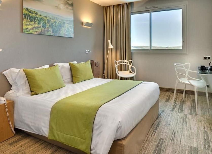 Le Panoramic Sancerre guest room with king bed, green accents, desk and window view