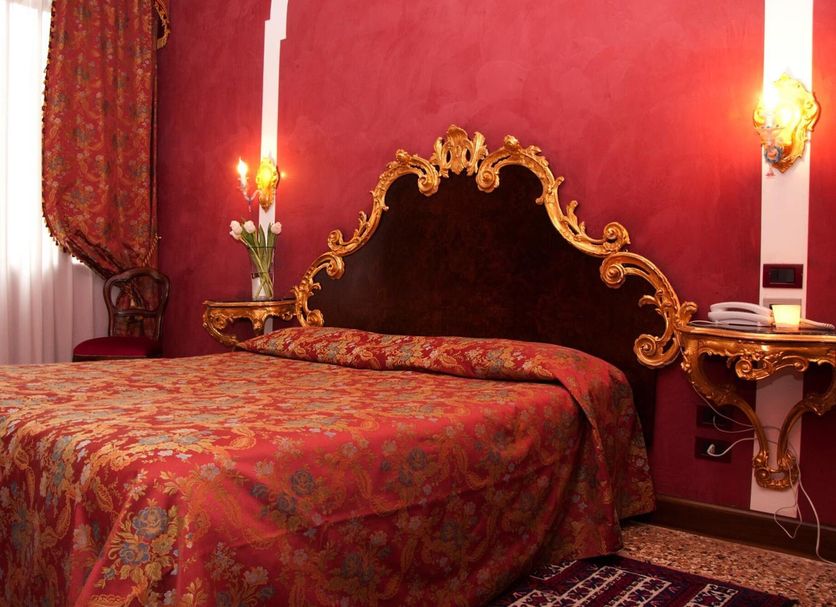 Residenza d'Epoca San Cassiano in Venice, ornate red guest room with gilded headboard and canopy bed