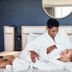 Hotel SLC in Murray: couple relaxing on a bed in a modern guest room with round mirror and blue wall