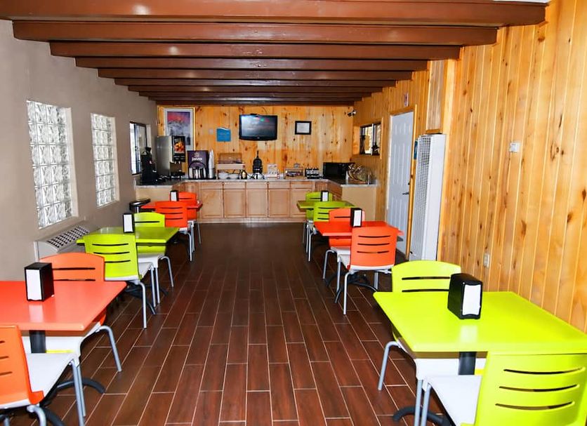 Budget Lodge Ruidoso dining area with colorful tables and chairs, wood-paneled walls, and a breakfast counter
