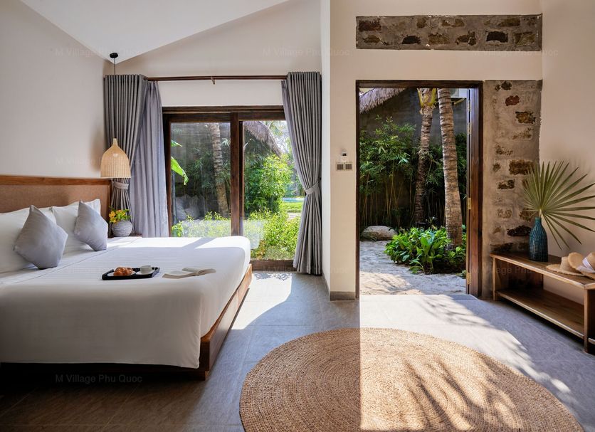 M Village Phu Quoc room with bed and sliding glass doors opening to a lush garden patio