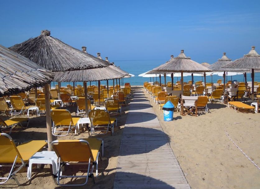 Hotel Loukas Vrachos beach loungers and thatched umbrellas on sandy shore in Vrachos, sea view