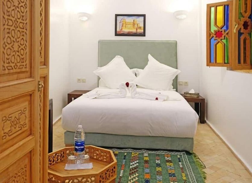 Riad Zanouba in Marrakech guest room with a bed, patterned rug, carved wooden doors, and colorful window