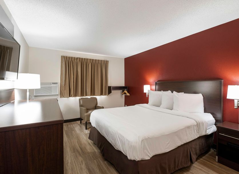 Red Roof Inn Bristol guest room with king bed, red accent wall, desk, TV and window air conditioner
