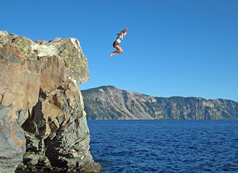 Riverside Inn, Grants Pass: person jumping from a rocky cliff into blue water with mountain backdrop