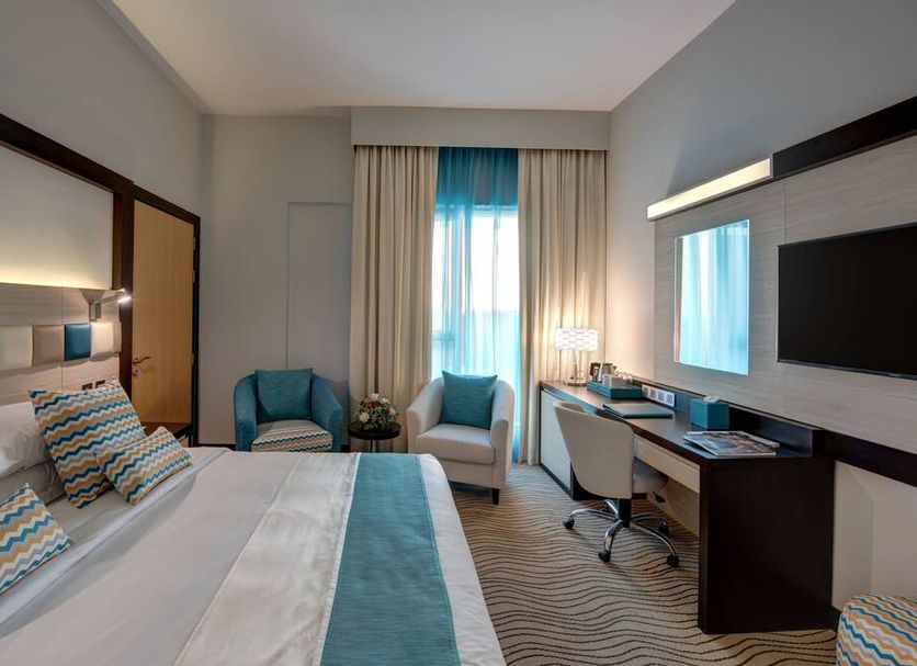 City Avenue Hotel Dubai room with king bed, desk, chair, window, and TV