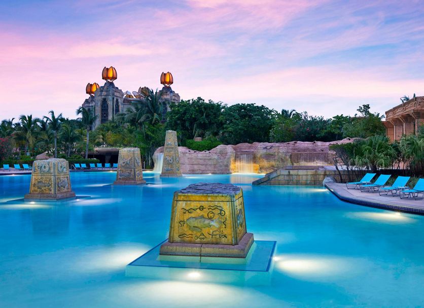 The Cove at Atlantis, Nassau: lagoon-style pool with stone columns, lounge chairs and pink sunset sky