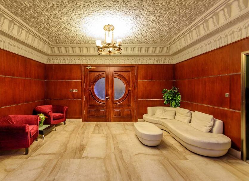 Arabella Residence Cairo lounge with curved cream sofa, red armchairs, ornate ceiling and wood-paneled walls