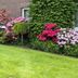 Hotel zum Rosenteich in Bad Zwischenahn with a lush lawn and colorful blooming flower shrubs by the brick exterior.