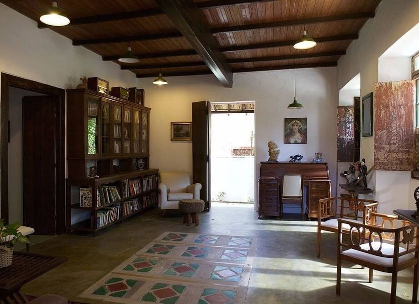 Pousada Irradiante in Olinda: rustic lounge with wood ceiling, bookshelves, chairs and patterned rug