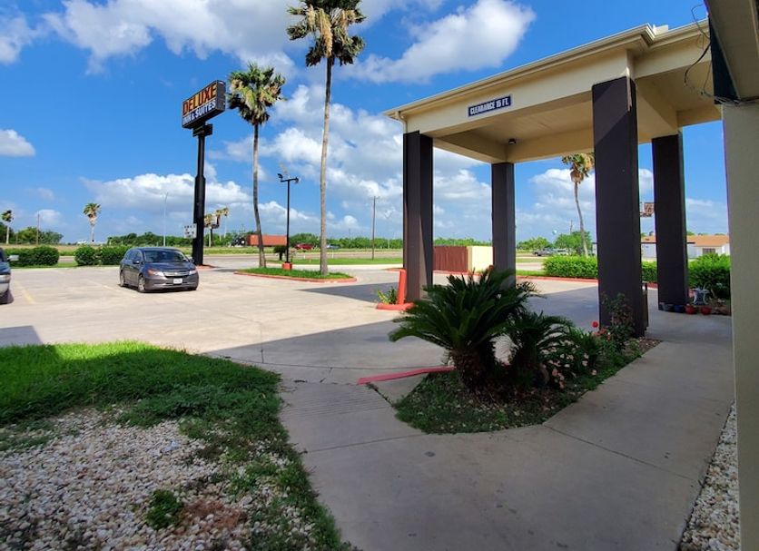 Deluxe Inn & Suites in Raymondville entrance with palm trees, driveway and blue sky