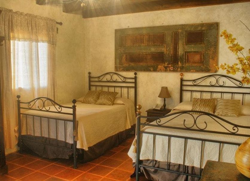 Las Iglesias Antigua guest room with two wrought-iron beds, tiled floor, and window curtains