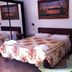 Agave Alghero guest room with floral bedspread, wall art, and green chairs