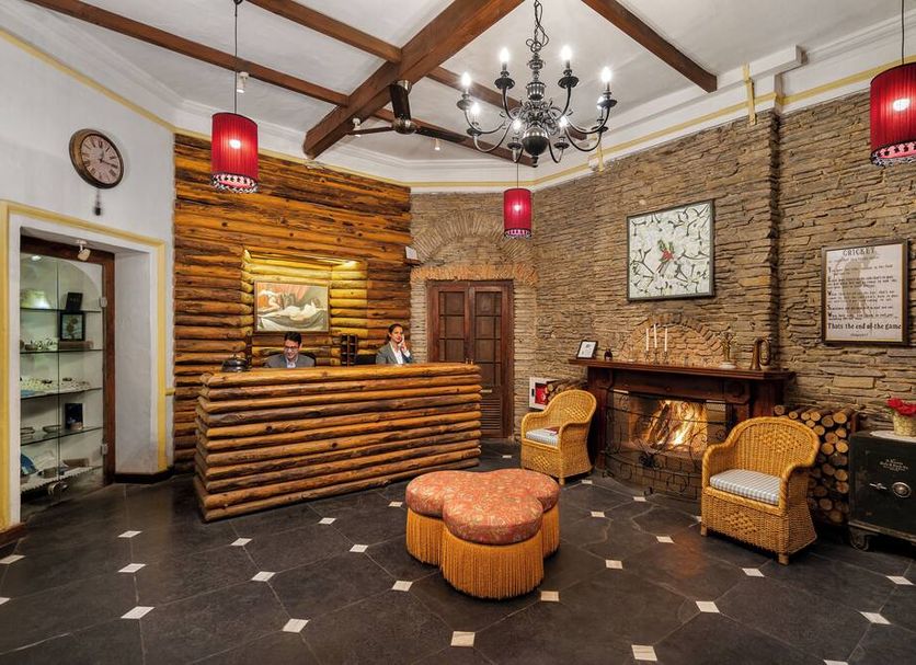 Rokeby Manor in Mussoorie lobby with stone fireplace, chandelier, wood reception desk and wicker chairs