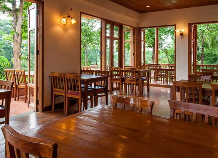 Riverhouse Resort in Mae Sariang dining room with wooden tables, chairs, and forest views