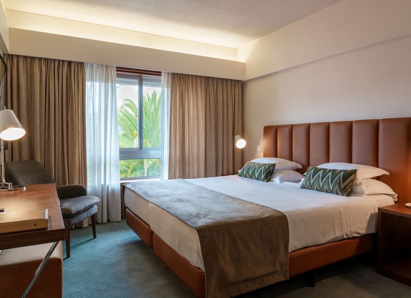 Hotel Dom Goncalo & Spa in Fátima guest room with king bed, desk, chair and window with palm view