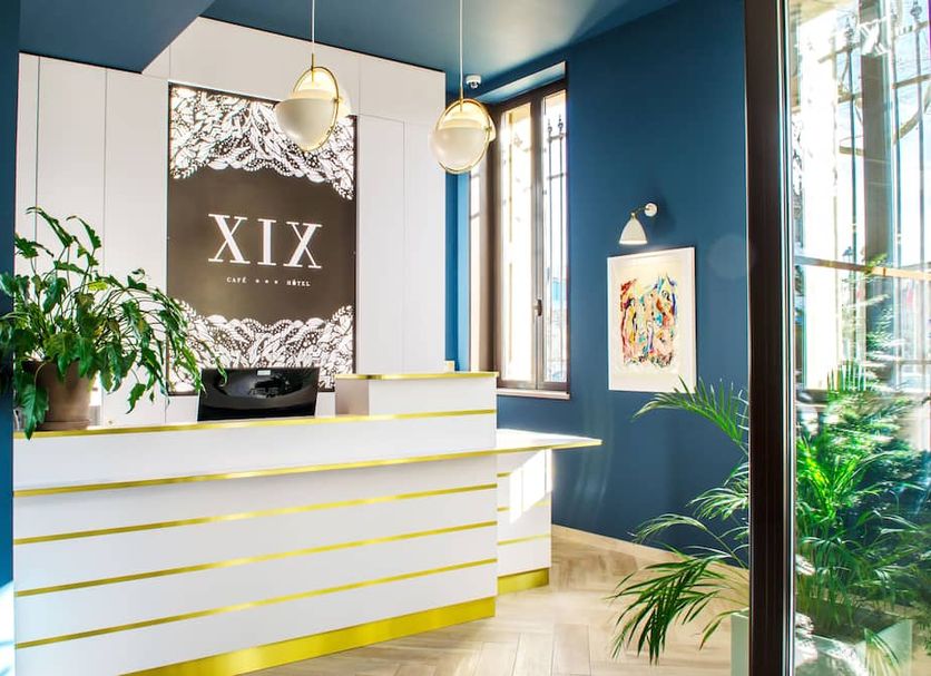 Hôtel Le XIX Béziers lobby with white reception desk, blue walls, pendant lights and potted plants