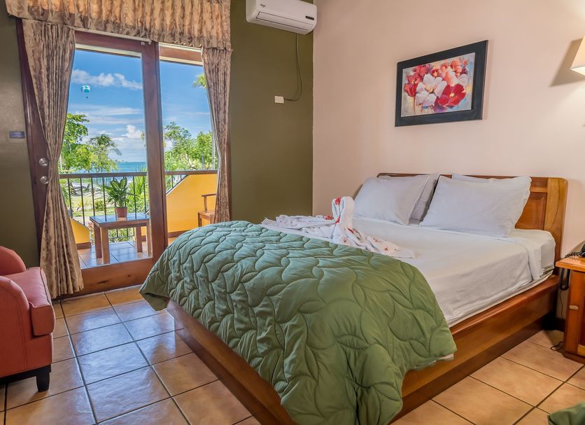 Hotel Manuel Antonio room with king bed, balcony doors, and tropical ocean-view greenery in Manuel Antonio