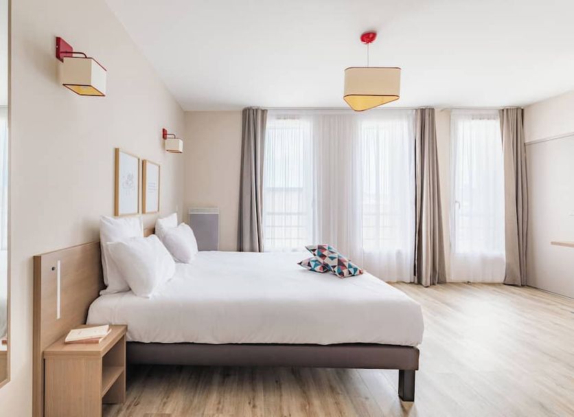 Appart'City Confort Cherbourg bedroom with large bed and sheer curtains in Cherbourg-en-Cotentin
