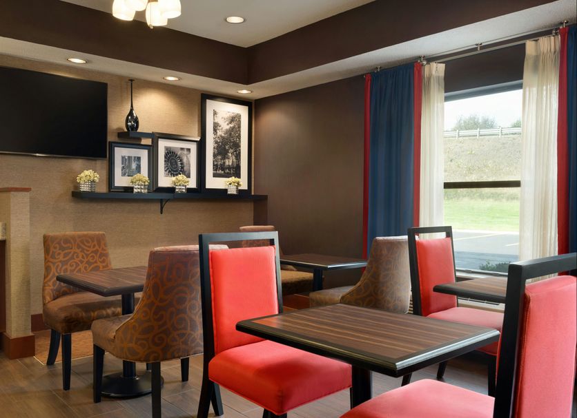 Hampton Inn Battle Creek lounge with tables and red chairs beside a large window