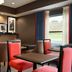 Hampton Inn Battle Creek lounge with tables and red chairs beside a large window