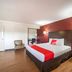 OYO Hotel Mcallen Airport South guest room with red accent wall, queen bed, chair, and wood flooring in McAllen