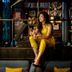 Woman in yellow outfit sitting on bar counter at Hotel G Yangon, with stylish lounge decor and shelves behind