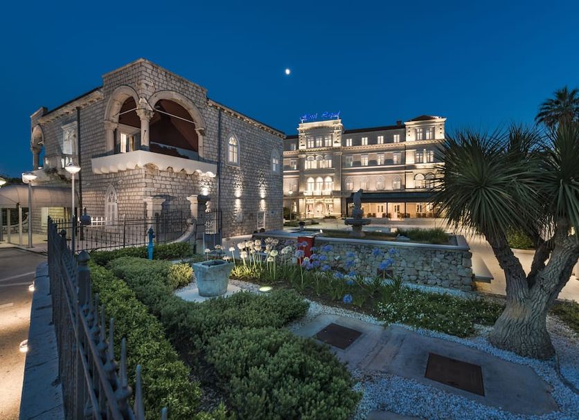 Hotel Lapad in Dubrovnik at night with a lit historic stone building, garden, and palm tree