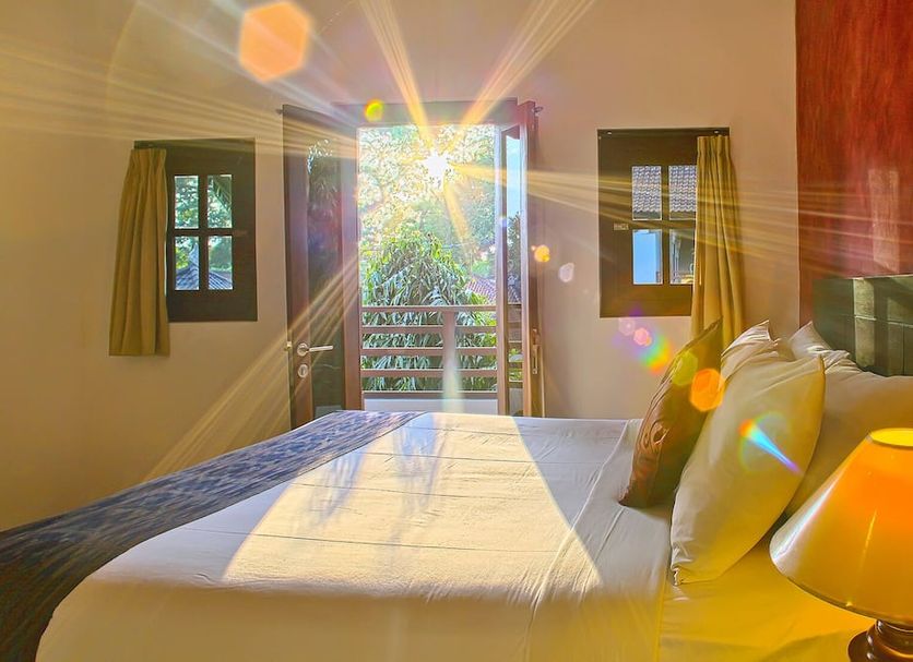 Puri Sading Hotel in Denpasar guest room with bed, lamp and open balcony doors to greenery