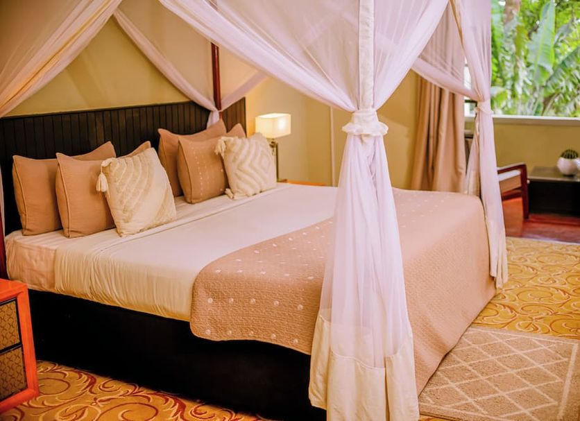 Heritage By Serendib in Blantyre, four-poster canopy bed beside a window with lush greenery