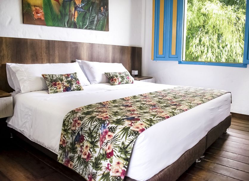 Hotel Hacienda Santa Clara room with king bed, floral runner and bright blue window in Santa Rosa de Cabal