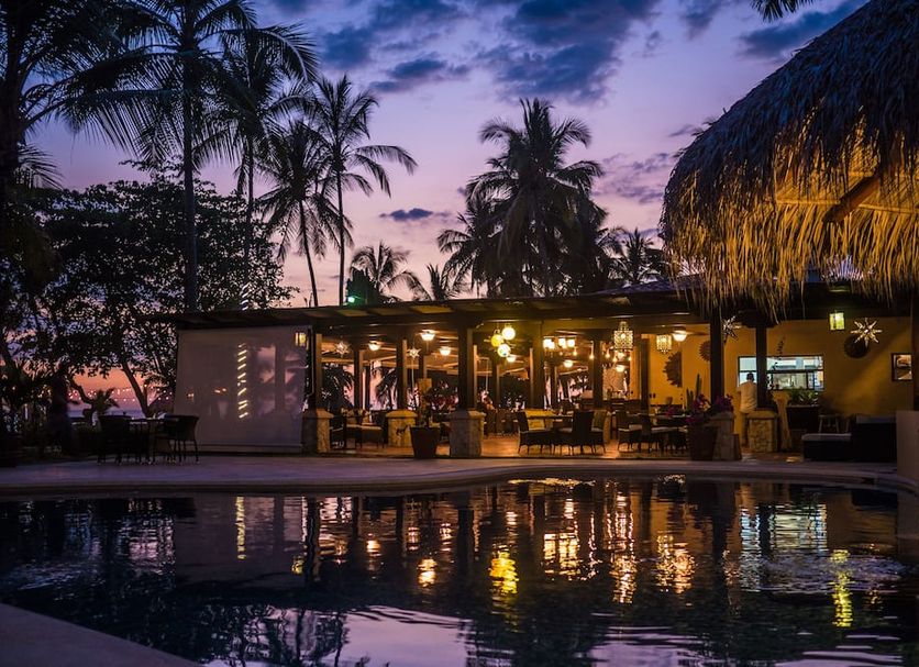 Sunset Del Mar Resort in Esterillos Este with lit poolside restaurant at dusk and palm trees