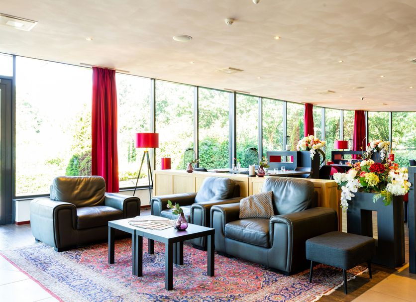 Bastion Hotel Roosendaal lobby with leather seating, red accents and large garden-view windows