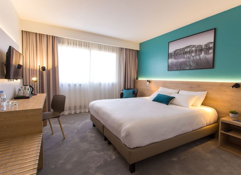 Hotel des Congrès Lyon guest room with king bed, desk, window light and teal accent wall
