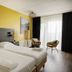 Strandhotel Vigilante in Makkum: modern twin bed room with yellow accent wall and seating by the window