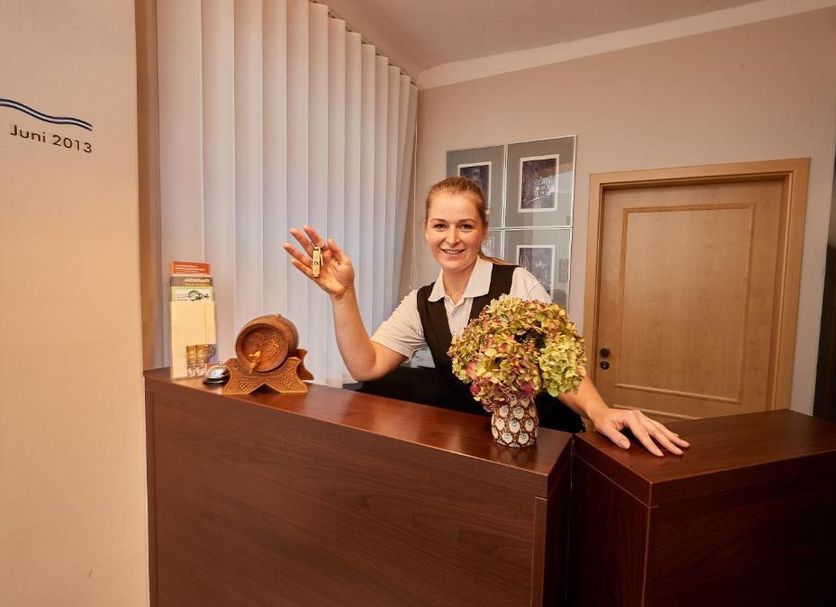 Am Malerweg, Pirna: smiling receptionist at wooden front desk with flowers in a cozy lobby