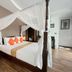 Jingjit Hotel Krabi bedroom with four-poster bed, white canopy, orange pillows and wood flooring