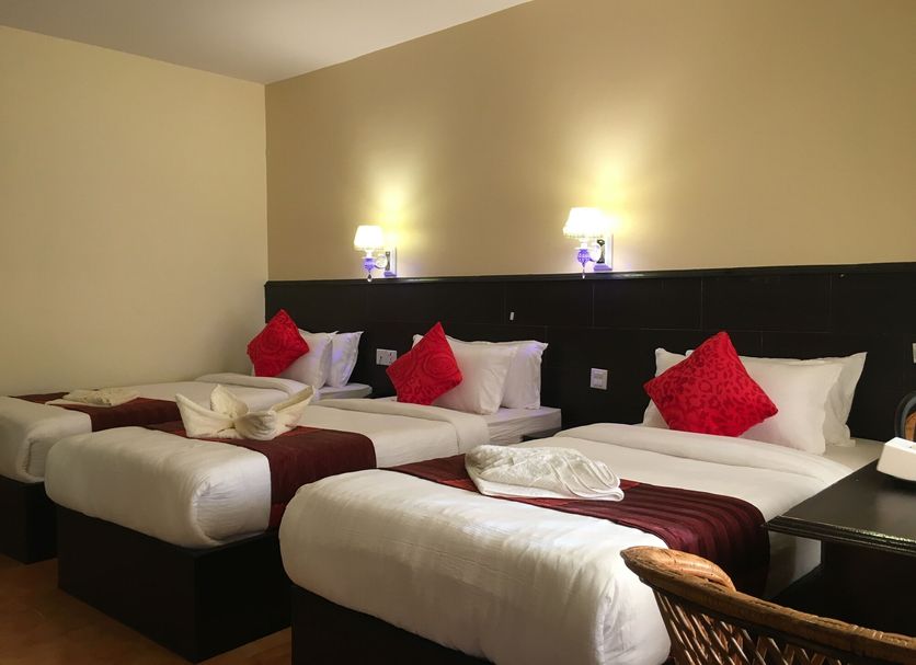 Katero in Pokhara: three neatly made twin beds with red accent pillows and wall lamps