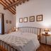 Le Rocche di Valiano guest room with wrought-iron bed, wood-beamed ceiling and window view