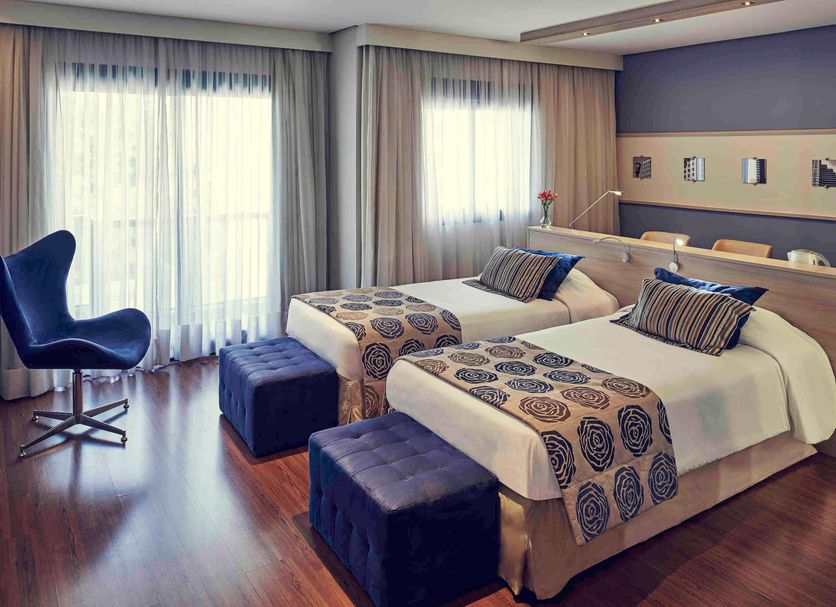 Mercure Sao Paulo Pamplona guest room with two twin beds, desk chair, and floor-to-ceiling window in Sao Paulo