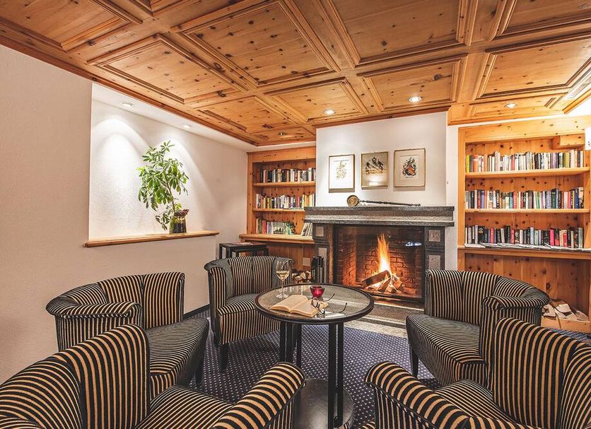 Hotel Post Sils Maria cozy lounge with fireplace, bookshelves and striped armchairs in Sils im Engadin/Segl