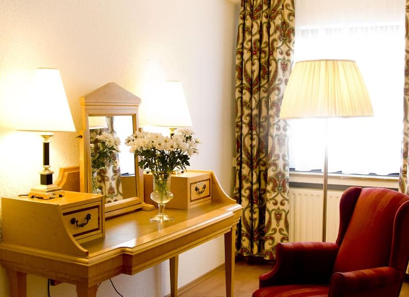 Hotel Kölner Hof Refrath room with desk, lamps, flowers, and red armchair in Bergisch Gladbach