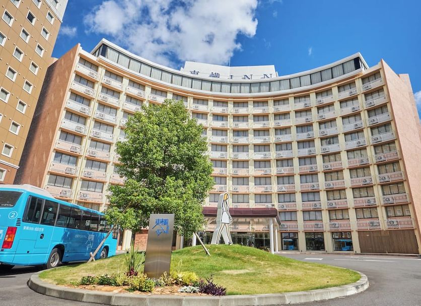 Toyoko Inn Narita Airport Honkan in Narita with curved facade, landscaped entrance, and blue shuttle bus