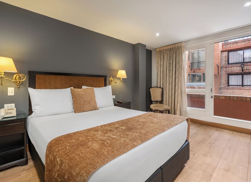 Le Manoir Bogota in Bogotá: guest room with king bed, bedside lamps, chair, and city-view window