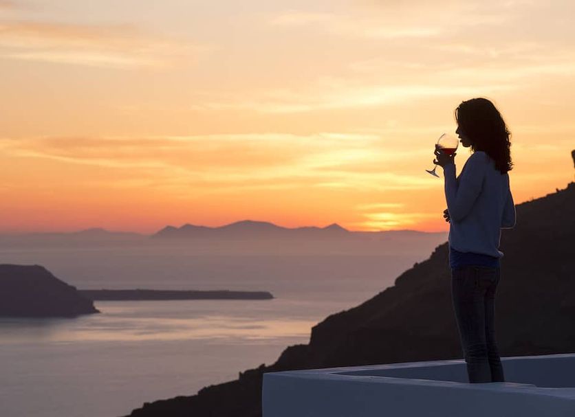 Alta Vista Suites, Thera: guest enjoying wine on terrace with sunset sea and caldera view